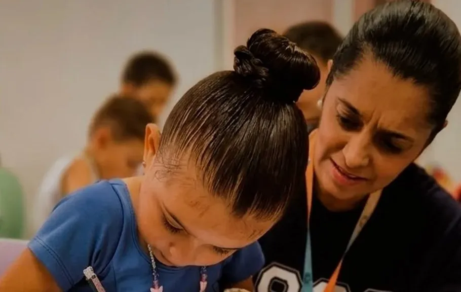 Aluna pequena escreve no caderno com a ajuda da professora